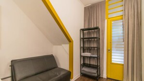 Una habitación pequeña con un sofá, una estantería metálica y una puerta amarilla.