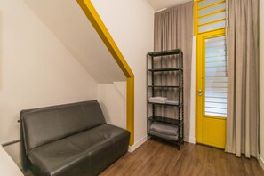 Um quarto pequeno com um sofá, uma estante de metal e uma porta amarela.