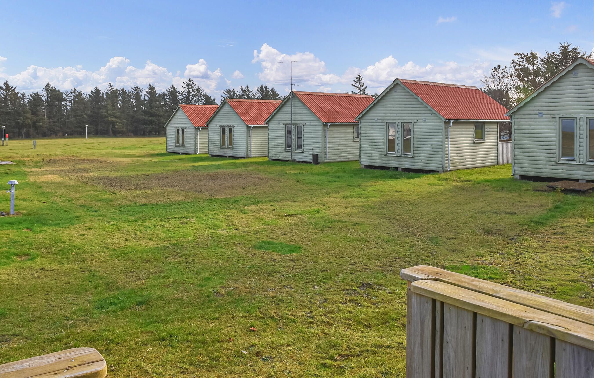 A row of small, light green cabins with red roofs, arranged in a grassy field with trees in the background.