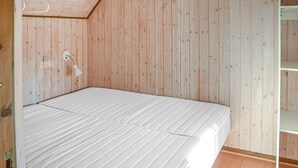 Une chambre avec un lit simple, des murs en bois, un matelas blanc et une lampe de chevet.