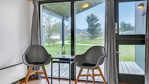 A room with two chairs and a table, large windows with curtains, and a view of a grassy area and trees. - Gorgeous home in Hanstholm with swimming pool (Hanstholm)