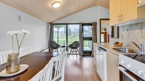 Eine moderne Küche mit Holzbalkendecke, einem Essbereich mit zwei Stühlen und Blick ins Freie durch große Fenster.