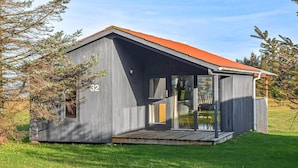 Eine kleine, eingeschossige Holzhütte mit rotem Dach, Nummer 32, in einer grünen Umgebung mit Bäumen.