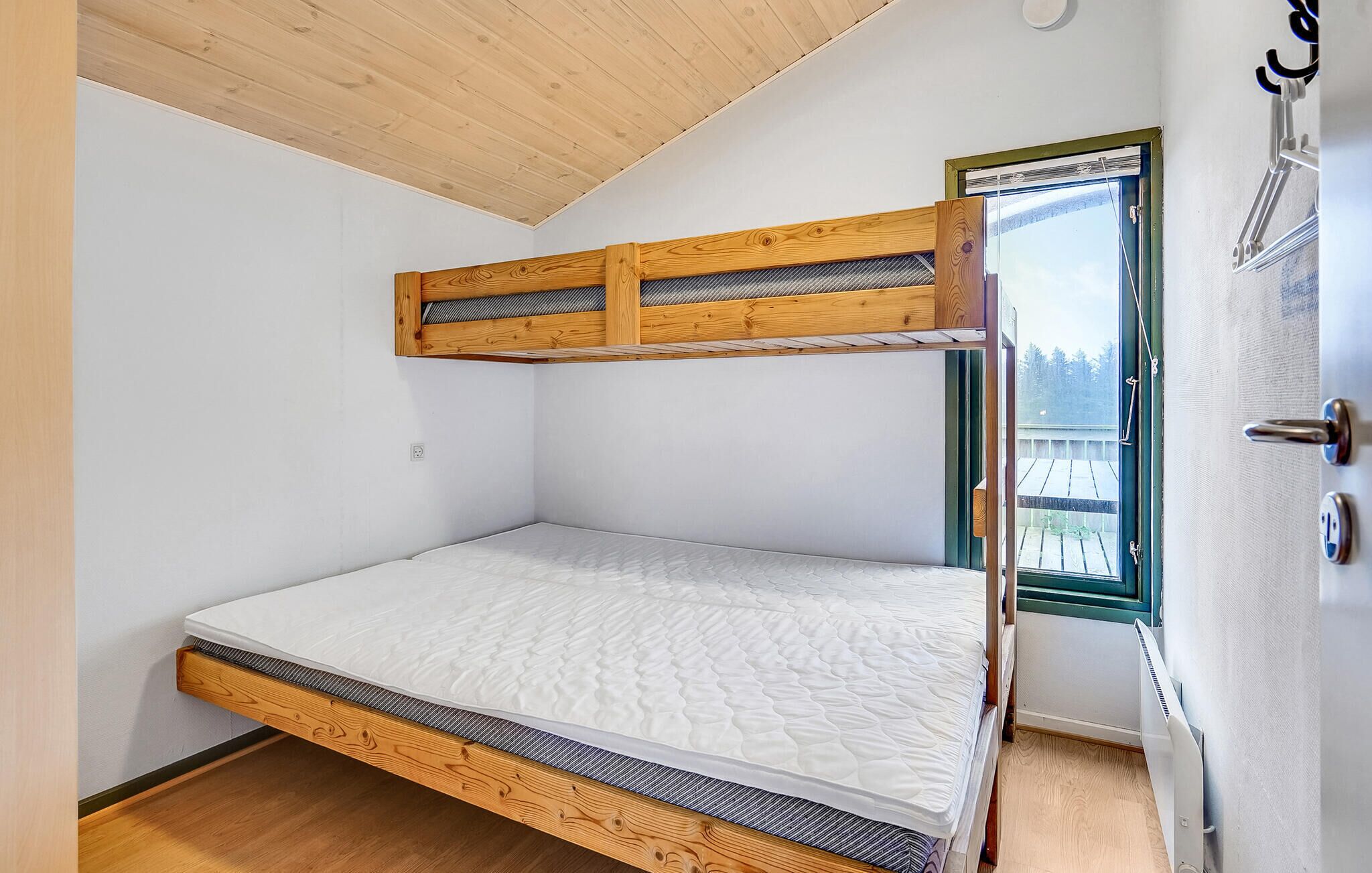 A bunk bed with a wooden frame and a mattress, a door with a window, and a ceiling with wooden beams.