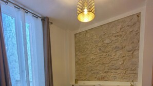 Un dormitorio con una cama grande, una pared de piedra, una lámpara colgante y una ventana con cortinas.