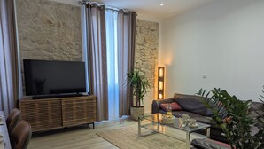 Una sala de estar moderna con un televisor de pantalla plana, mueble de entretenimiento de madera, sofá de cuero, mesa de centro de vidrio y una pared decorativa de piedra.