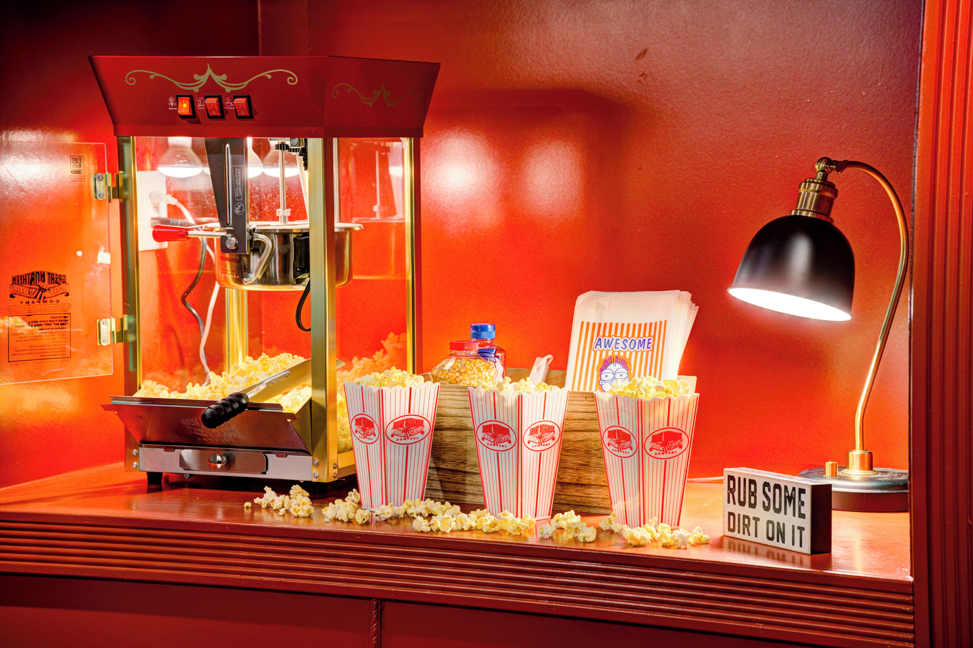 Una máquina de palomitas de maíz con exterior rojo, un recipiente para palomitas y un letrero que dice "RUB SOME DIRT ON IT".