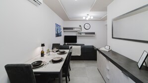 A modern, minimalist dining area with a white table set for two, a black sofa, and a built-in TV. - La Boutique Apartment - Borgo Delle Colonne (Parma)