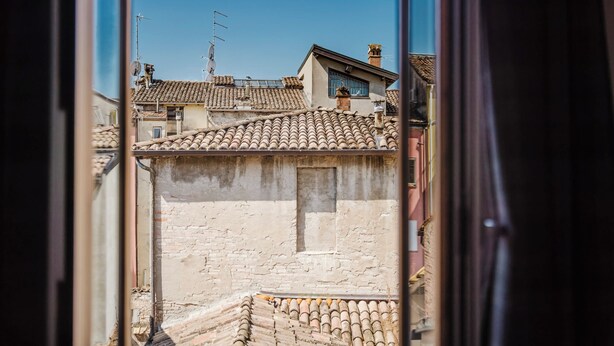 A view through a window of a building with a tiled roof, visible chimneys, and a clear blue sky. - La Boutique Apartment - Borgo Delle Colonne (Parma)