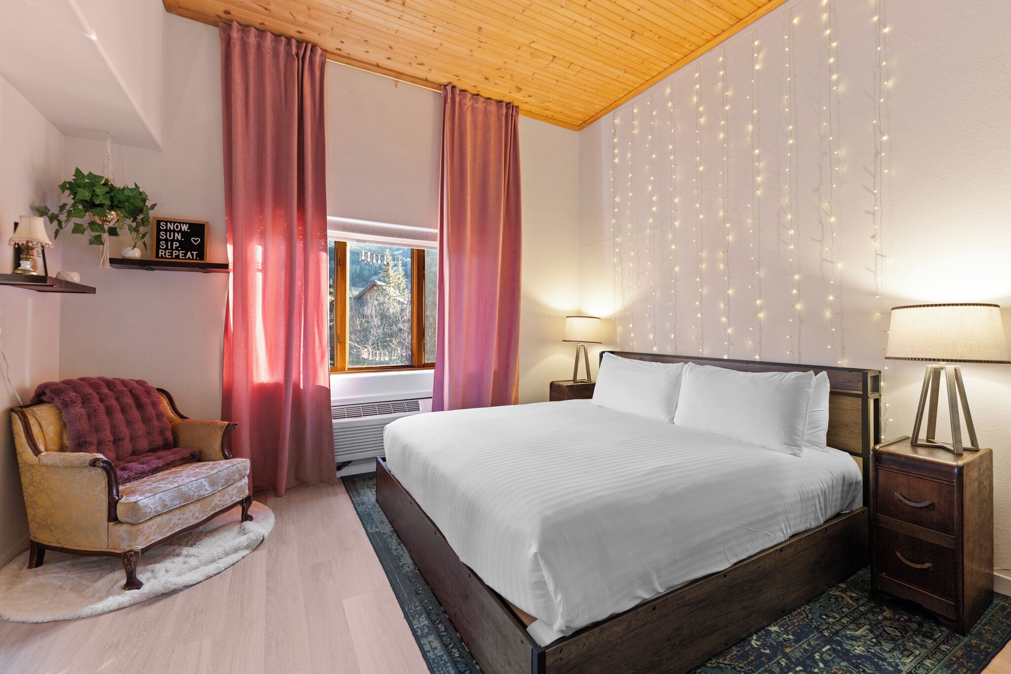 A cozy bedroom with a wooden bed, a chair, a nightstand, and a window with curtains.