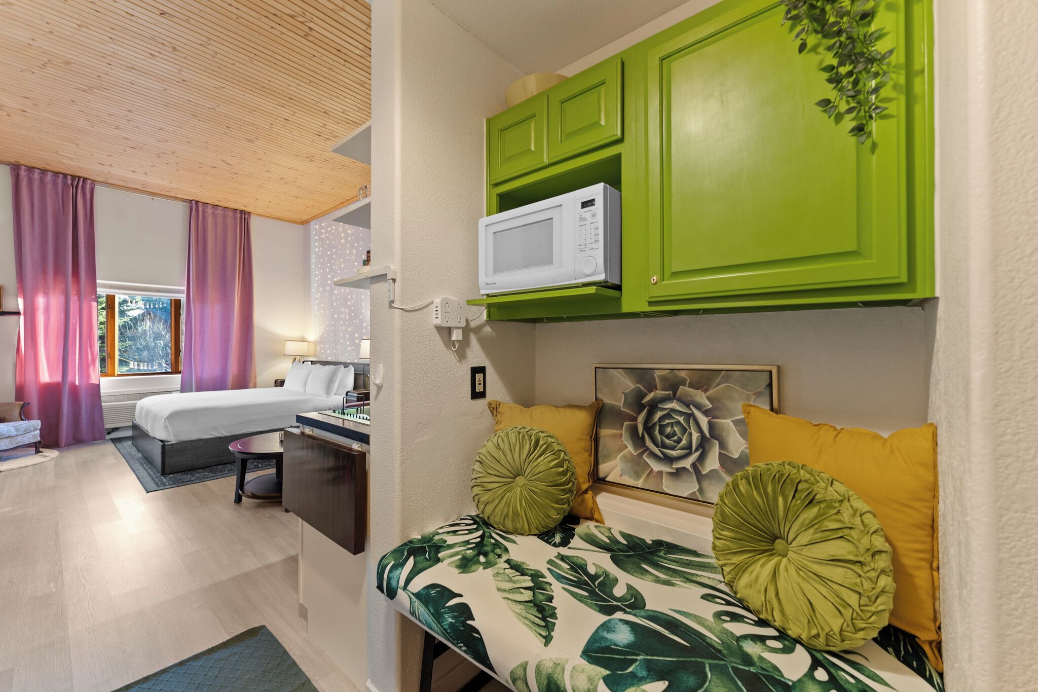 A hotel room with a bed, a desk, a microwave, and a green cabinet.