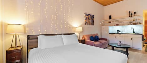 A hotel room with a large bed, bedside lamps, a sofa, a small table, and a kitchenette.