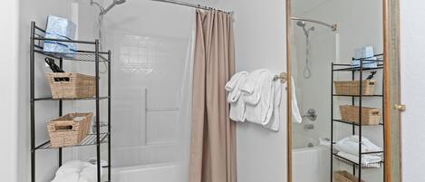 A bathroom with a shower, a bathtub, and a mirror. There are shelves with baskets and towels.