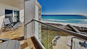 A balcony with two lounge chairs, a view of the beach, and a pool area with sun loungers. - Regency Towers #401 East - Sea La Vie (Pensacola Beach)
