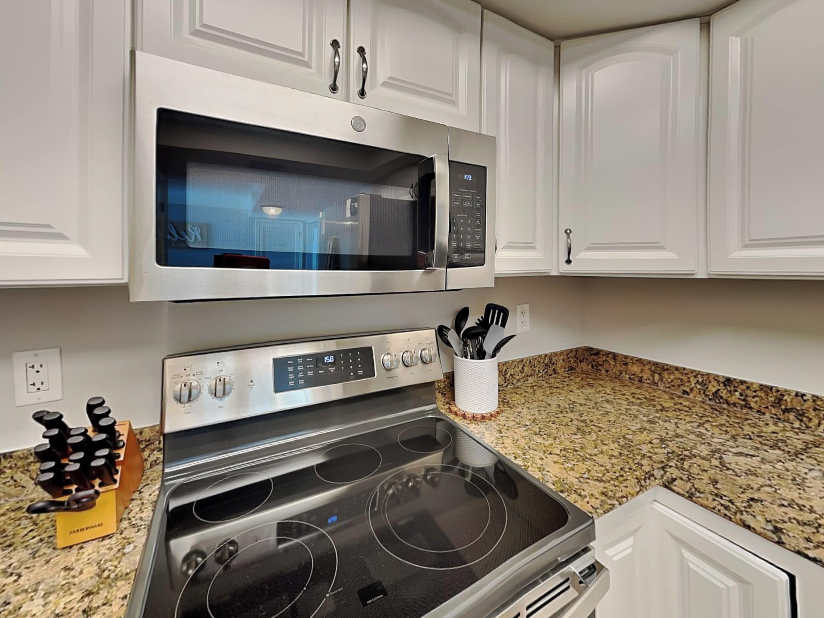 A kitchen with white cabinets, a stainless steel microwave, an oven, and a granite countertop.