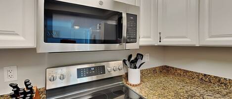 A kitchen with white cabinets, a stainless steel microwave, an oven, and a granite countertop.