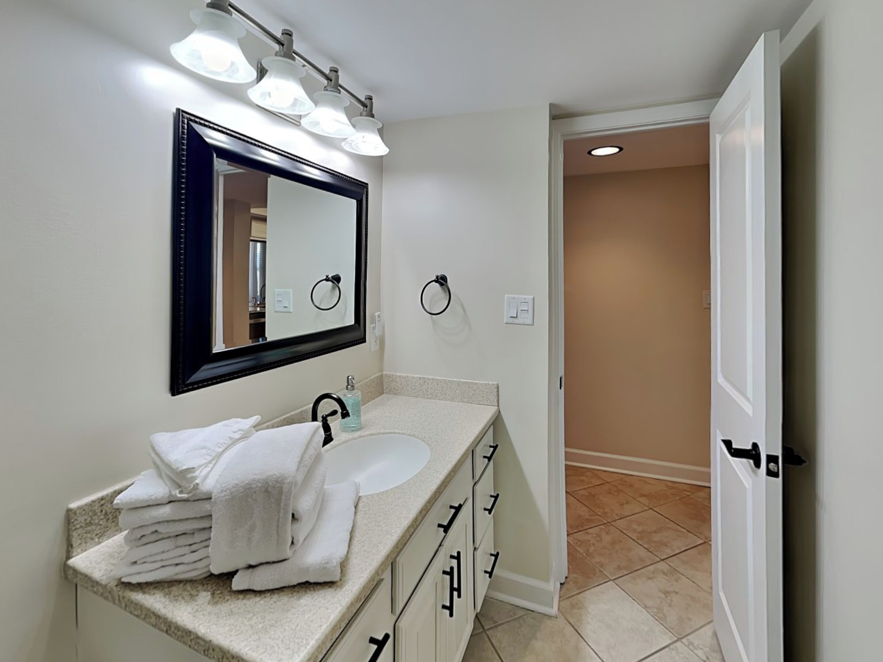 A bathroom with a sink, mirror, towel stack, and a door leading to another room.