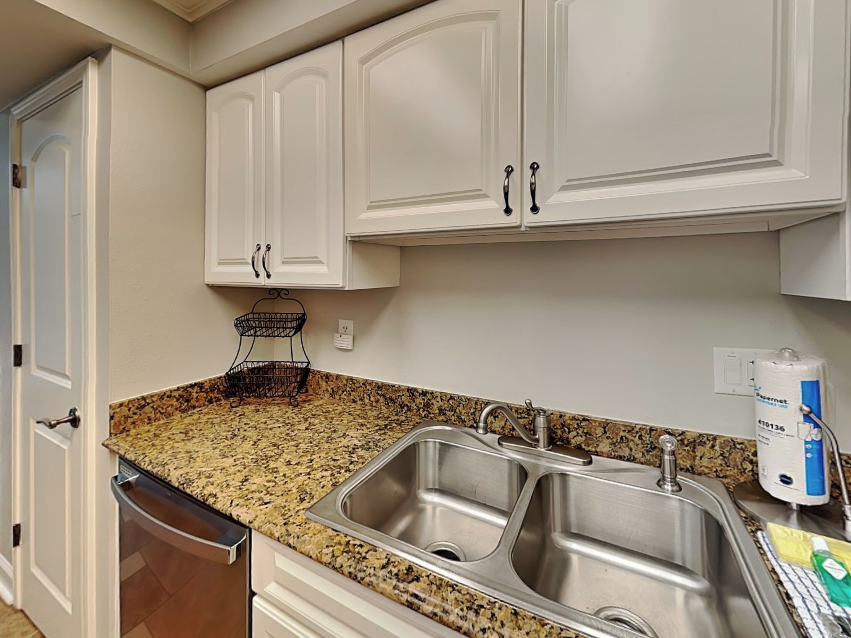 A kitchen with white cabinets, a granite countertop, and a double sink.