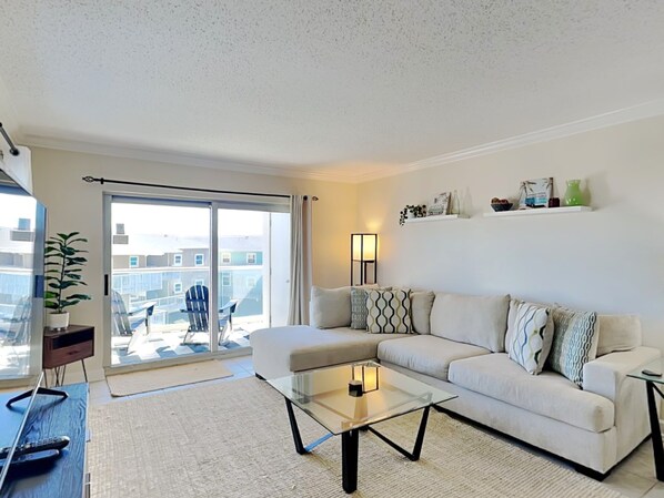 Ein modernes Wohnzimmer mit einer Couch, einem Glastisch, einem Fernseher und einem Balkon mit einem Stuhl.
