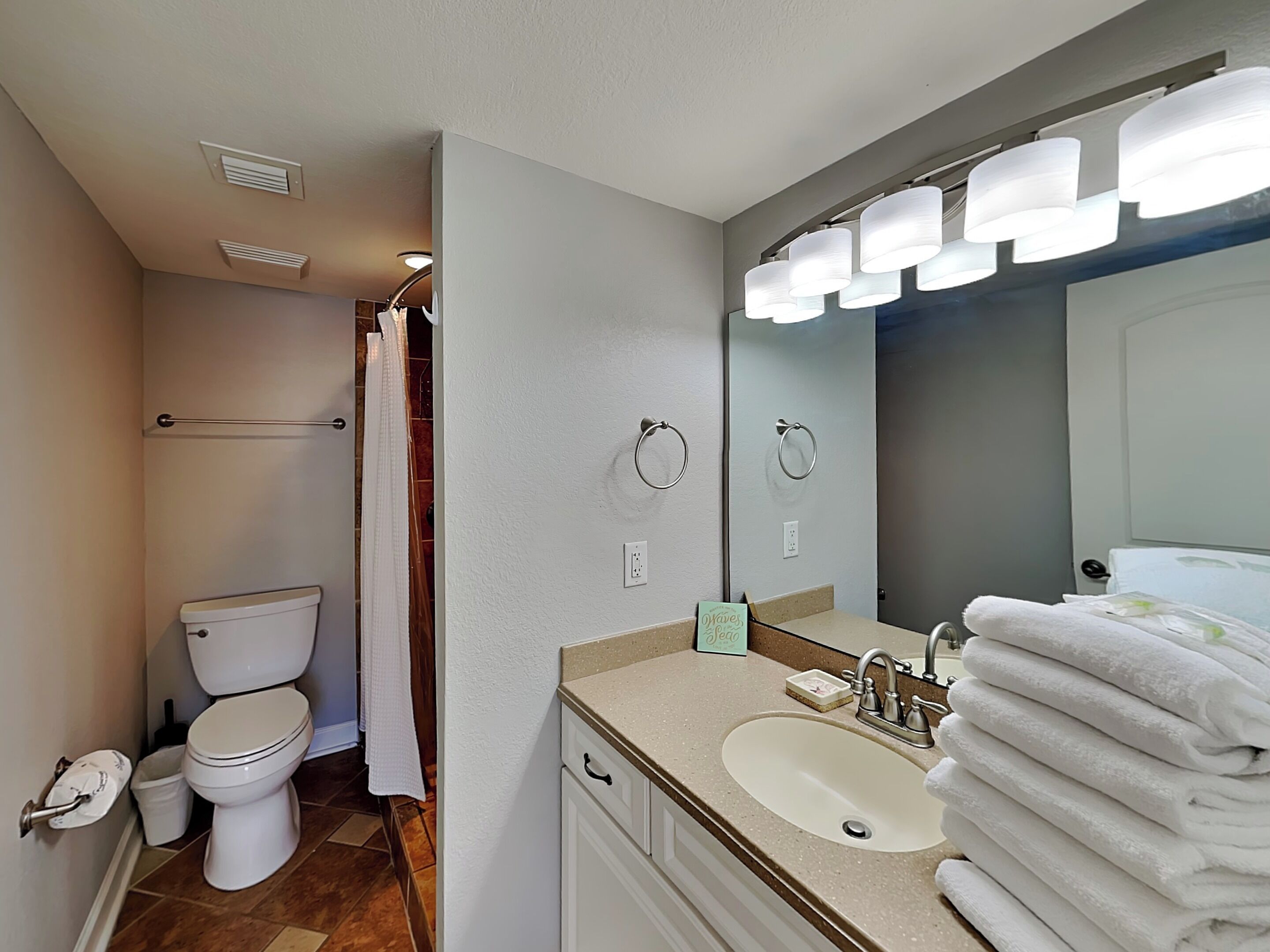 A bathroom with a toilet, sink, mirror, towel rack, and a towel stack.