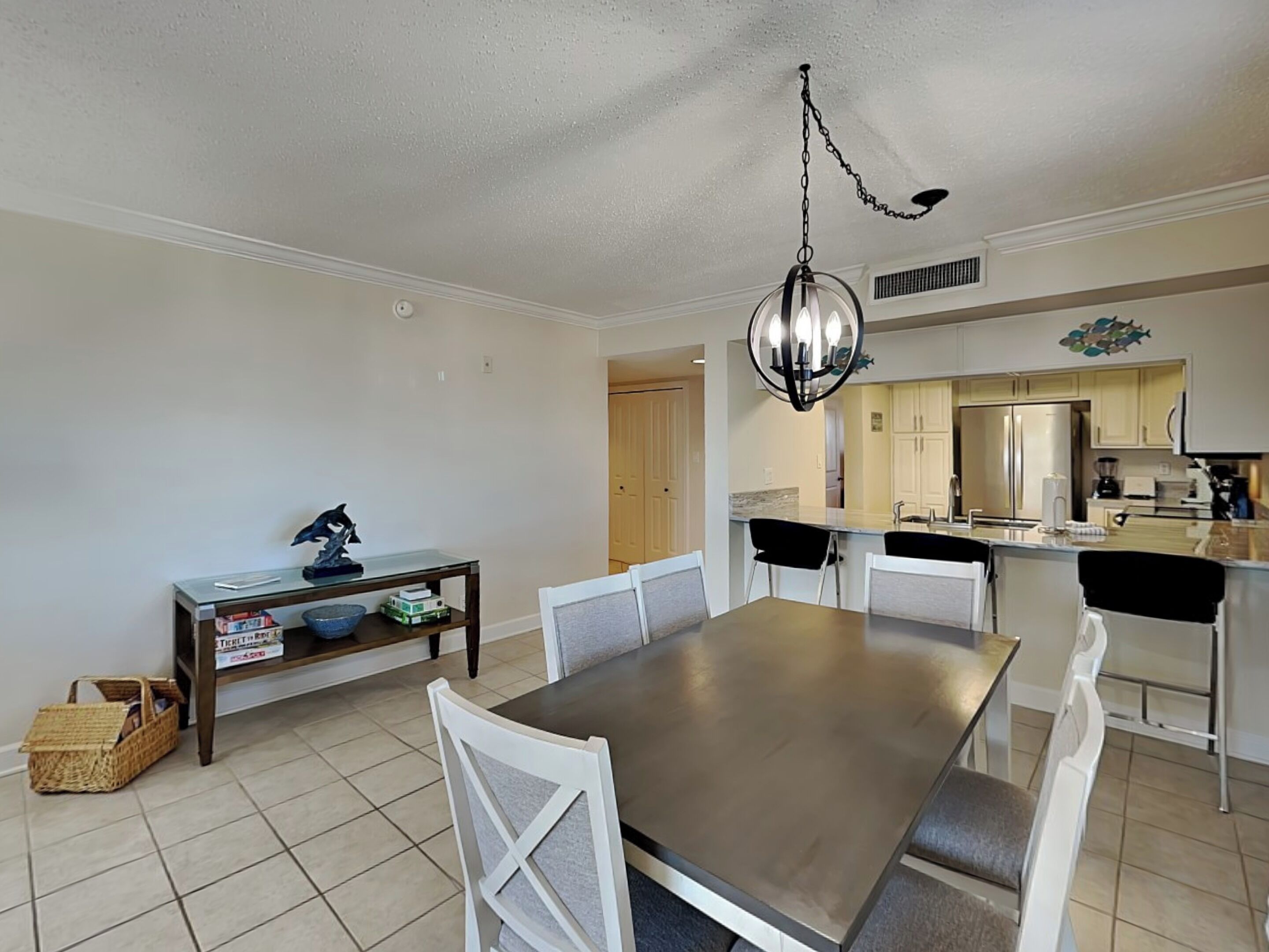 A dining area with a rectangular table and six chairs, a chandelier, and a kitchen in the background.