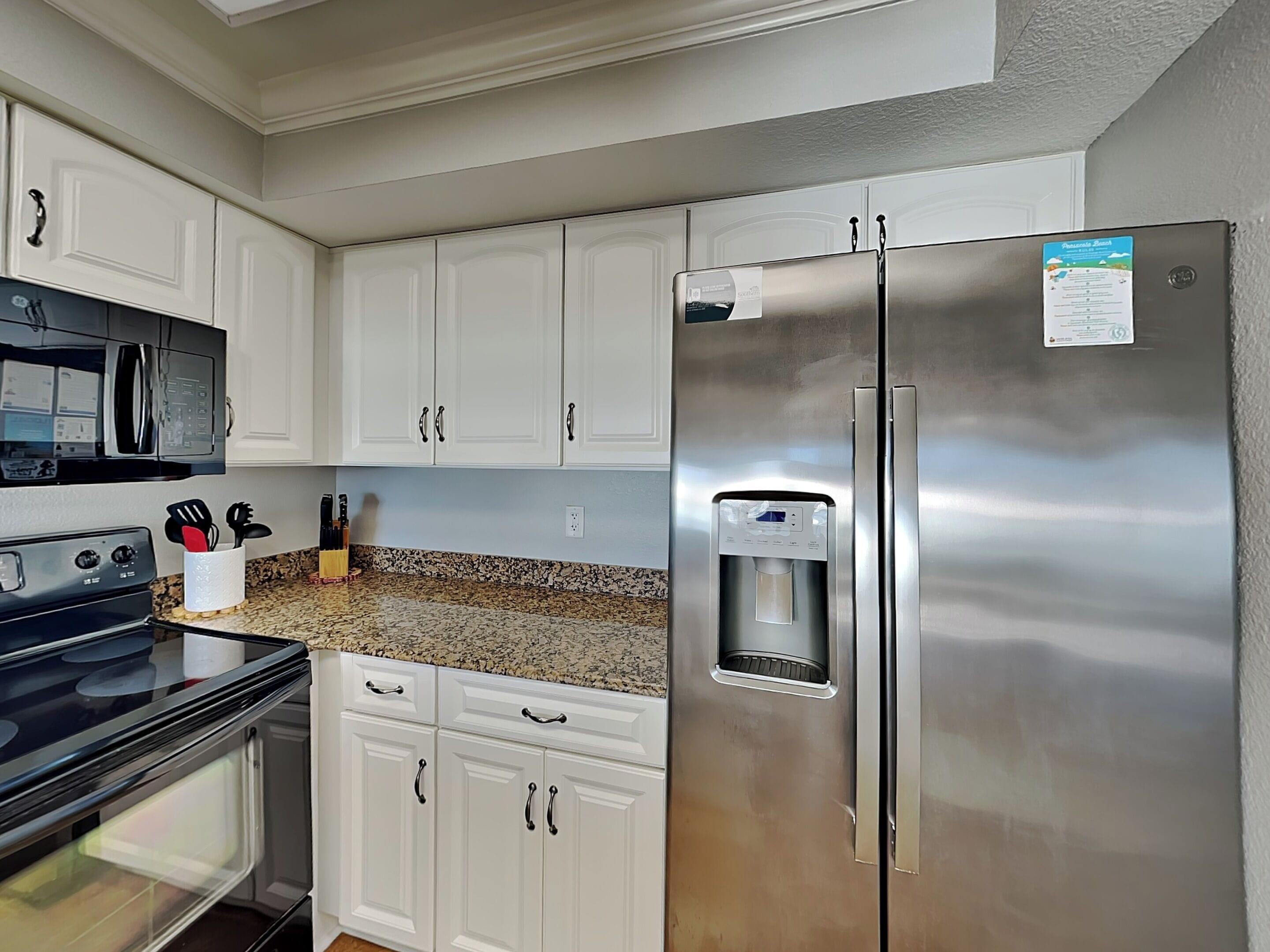 A kitchen with white cabinets, a stainless steel refrigerator, a microwave, and a water dispenser.