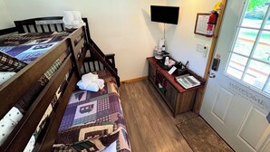 Een kleine kamer met een stapelbed, een bureau met een computer, een lamp en een deur met een 'Welcome' bordje.