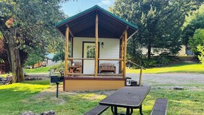 Een rustieke blokhut met een veranda, houten stoelen en een picknicktafel.