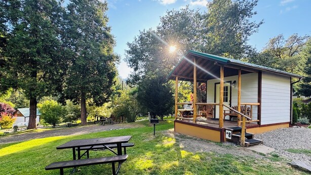 Een rustieke blokhut met veranda en picknicktafel in een bebost gebied.