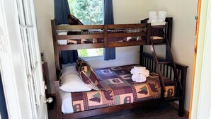 Een stapelbed met een bedspread met patroon, kussens en een klein tafeltje met handdoeken.