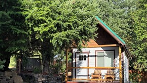 Une cabane avec un mur en pierre, une terrasse en bois et deux chaises.