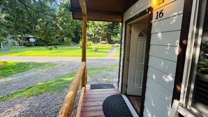 A wooden porch with a number 16 sign, a gravel path, and a grassy yard with trees.