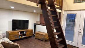 Ein Wohnzimmer mit einer Holzeinrichtungsanlage, einem Fernseher, einer Couch, einer Holzleiter und einer Tür mit Jalousien.