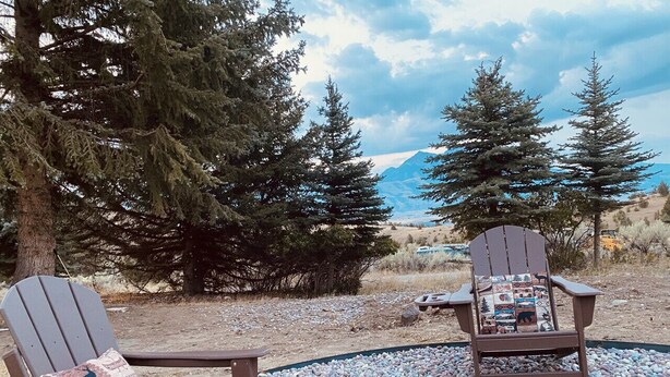 Zwei Adirondack-Stühle mit farbigem Sitzkissen auf einem Kiesgrund, mit Blick auf Bäume und Berge im Hintergrund.