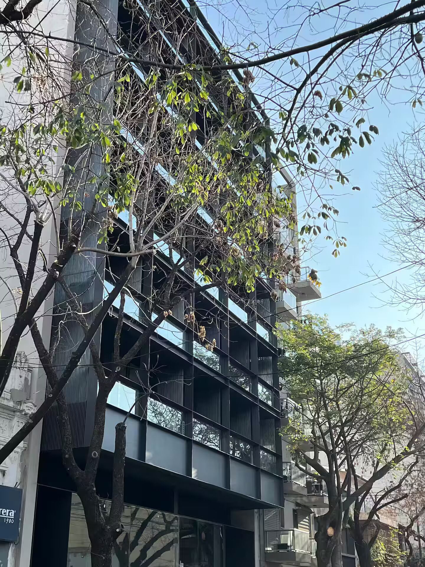 A multi-story building with a modern architectural design, featuring balconies and a mix of glass and metal elements.