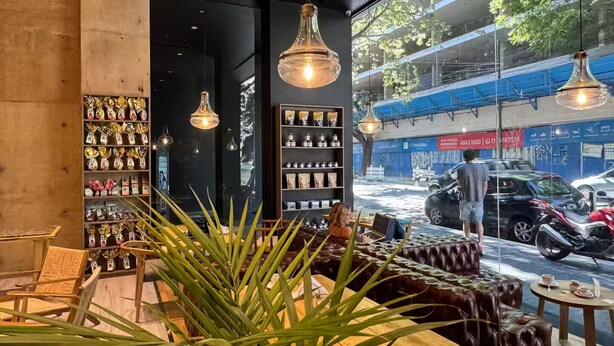 Un café chaleureux avec des fauteuils en cuir, une variété de produits emballés présentés sur des étagères et de grandes fenêtres donnant sur une rue animée.