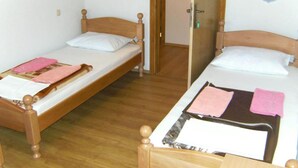 Zwei hölzerne Betten mit weißer und rosa Bettwäsche, eine Holztür und ein Lichtschalter an der Wand.