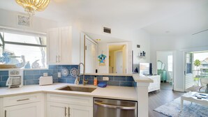 Una cocina moderna con armarios blancos, un lavavajillas de acero inoxidable y un ventanal decorado.