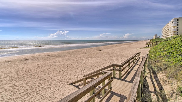 Una playa con un paseo marítimo de madera que lleva a un edificio con varios balcones.