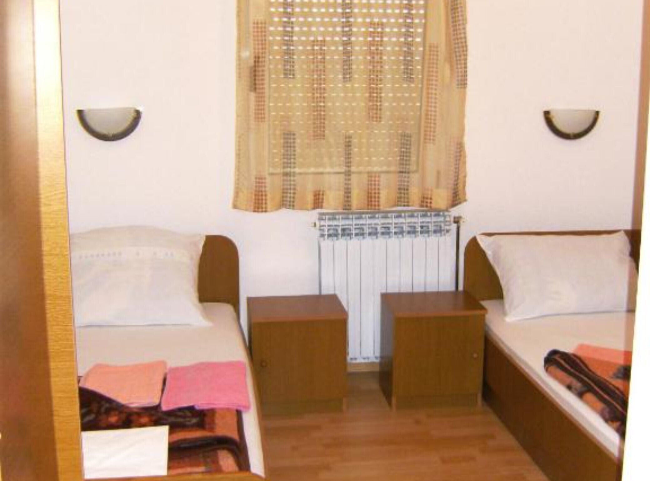 A small, compact room with two single beds, a radiator, and two wall-mounted lamps.