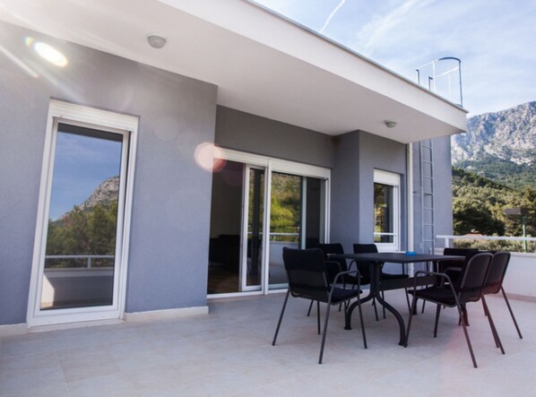 Une terrasse extérieure moderne, dotée d’une table et de chaises, de grandes portes-fenêtres coulissantes et offrant une vue sur les montagnes.
