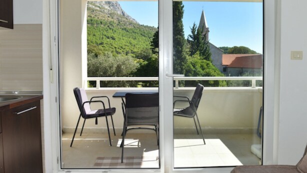 Un balcon avec une table et des chaises, une vue sur une montagne et une église, et une porte-fenêtre coulissante.