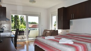 Une chambre à coucher avec un lit, un bureau et une chaise. Il y a un balcon d’où l’on peut admirer les arbres et les bâtiments.