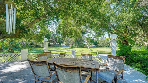 An outdoor patio with a table and chairs, surrounded by lush greenery and a view of a lawn and trees. - Explore Dtwn Sarasota & Beaches: Home w/ Lush Yard (Sarasota)