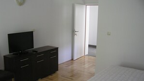 Ein Schlafzimmer mit einem Bett, einem Schminktisch, einem Fernseher und einer Tür zu einem anderen Raum.