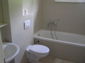 Een badkamer met toilet, toiletbrons en bad.