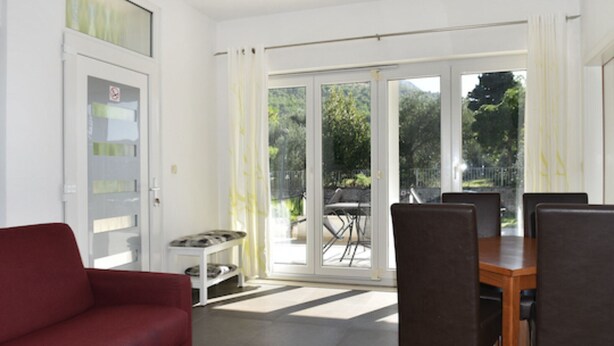 Una sala moderna con un sofá rojo, una mesa de comedor con sillas y un ventanal corredizo que da a un espacio exterior con una mesa y sillas de patio.