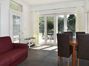 A modern living room with a red sofa, a dining table with chairs, and a sliding glass door leading to an outdoor area with a patio table and chairs. - Apartments Despot Zaostrog RC (Zaostrog)