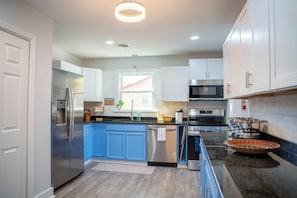 A modern kitchen with stainless steel appliances, blue cabinets, and a large window. - Beautifully Renovated 4 Bedroom Home; Fully Furnished & Move-in Ready. (Petersburg)