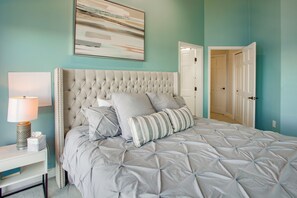 A bedroom with a tufted headboard, a bedside table with a lamp, and a bed with grey bedding. - Riverfront Fort Myers Luxury Home w/ Heated Pool! (Fort Myers)